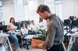 © standret - Stylish man in glasses holding box with plant in front of his colleagues in the office