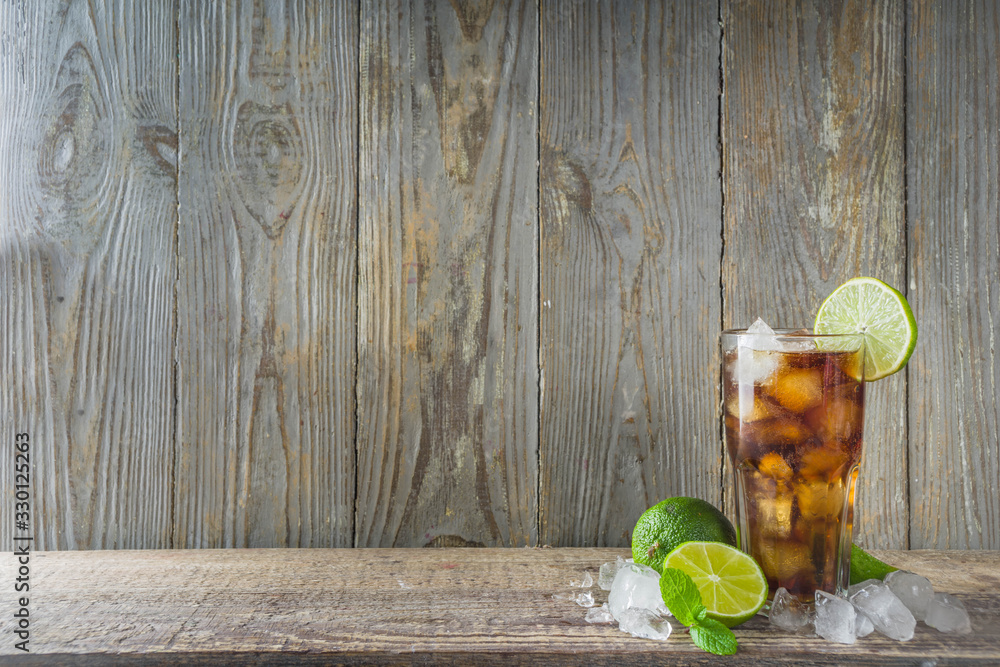 Summer iced alcohol drink with cola and lime. Rum and cola Cuba Libre cocktail. One long glass on wooden background copy space - obrazy, fototapety, plakaty 