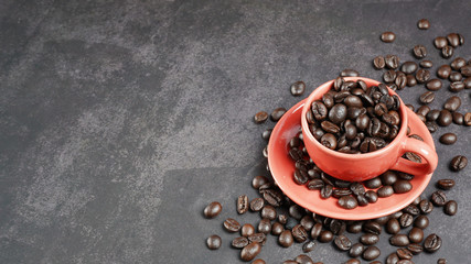 Roasted coffee beans in a red cup on black background.