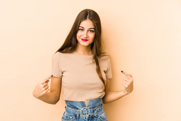 Young caucasian woman isolated en beige background person pointing by hand to a shirt copy space, proud and confident