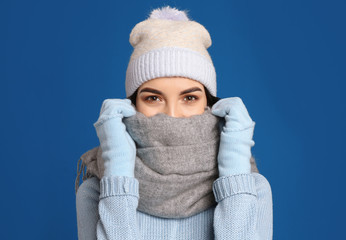 Poster - Young woman wearing warm sweater, gloves, scarf and hat on blue background. Winter season