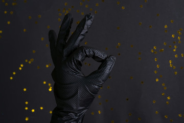 Woman's hand in a black latex glove for cleaning making an OK sign on the same color background.