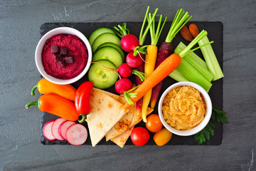 Wall Mural - Assortment of fresh vegetables and hummus dip on a serving platter. Above view on a slate background.