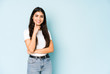© Asier - Young indian woman on blue background smiling happy and confident, touching chin with hand.