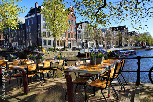 Restaurant tables lining the beautiful canals of Amsterdam under blue skies duri Canvas Print