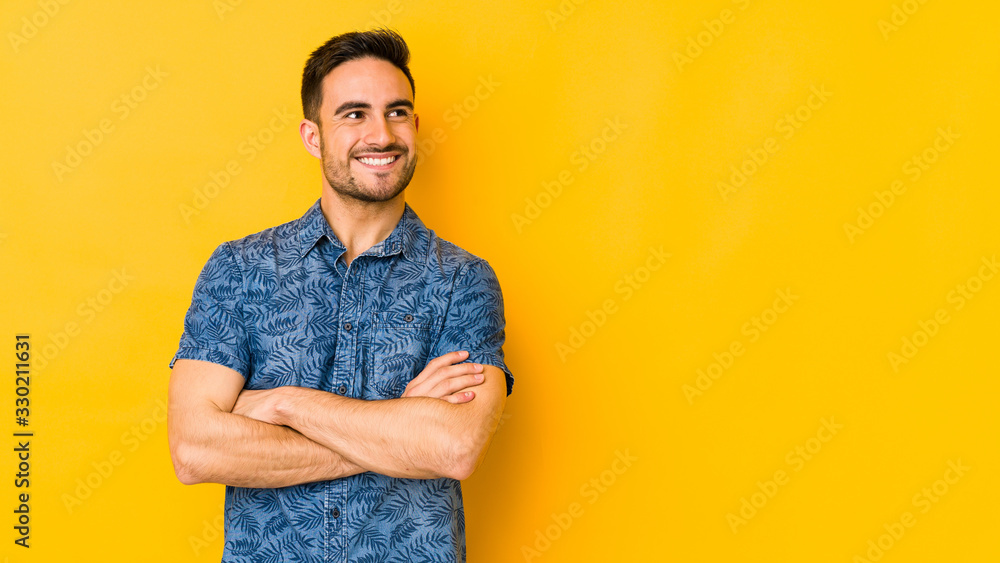 Young caucasian man isolated on yellow bakground smiling confident with crossed arms. - obrazy, fototapety, plakaty 