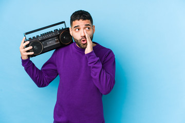 Wall Mural - Young arabian man holding a radio cassette isolated Young arabian man listening music is saying a secret hot braking news and looking aside