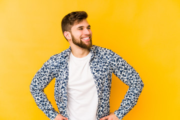 Wall Mural - Young caucasian man isolated on yellow background laughs happily and has fun keeping hands on stomach.