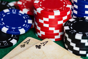 A pair of aces, Clubs and Spades, on well used vintage deck of playing cards, surrounded by Blue, Red and Black betting chips on a standard green felt playing surface.