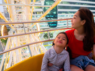 Wall Mural - happy asia mother and daughter have fun in amusement carnival park with farris wheel and carousel background