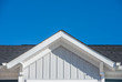 Gable roof with white fascia, gray vertical vinyl lap siding blue sky background