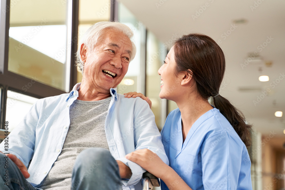 young friendly asian female caregiver talking to elderly man in nursing home - obrazy, fototapety, plakaty 