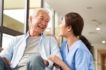 Canvas Print - young friendly asian female caregiver talking to elderly man in nursing home