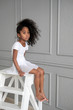 © evelinphoto - A portrait of an African ballerina in a white gymnastic costume sits on a wooden chair.