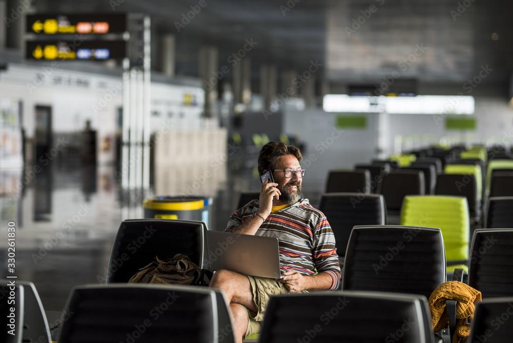Adult man travel at the airport sit down at the gate waiting for his airplan flight - delay conncept and people working everywhere with laptop computer technology - caucasian male traveling - obrazy, fototapety, plakaty 