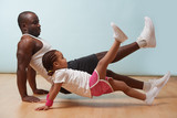 Handsome black young father and his cute little daughter are doing reverce plank with leg raise on the floor at home. Family fitness workout.
