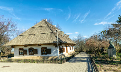 Wall Mural - Old traditional village house in the background of the garden. Clay white walls and plank roof