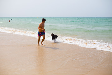 Hombre joven en verano disfrutando  del sol y playa junto a su perro 