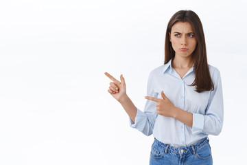 Wall Mural - Upset or jealous cute brunette woman in blouse pouting, sulking with regret, being offended not invited to cool office party, squinting and looking pointing left with disapproval, white background