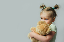 Portrait Of Baby Toddler Holding Soft Toy Looking Away On Gray Background. Children Rights Concept. Free Space For Text. 