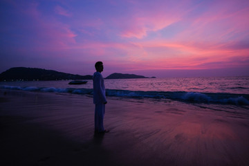 A man practices yoga on the ocean during a purple sunset.