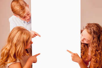 Wall Mural - Twoo cute child girls and one boy pointing with fingers towards copy space area. Free space for design. Horizontal image.