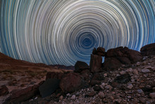 A Beautiful Night Sky Landscape With Circular Star Trails, And Interesting Rock Formations In The Foreground And Mountains On The Horizon, In The Richtersveld National Park, South Africa.