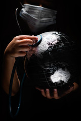 Wall Mural - kid hold globe put stethoscope on sphere, face covered in mask on black background. ecological probl