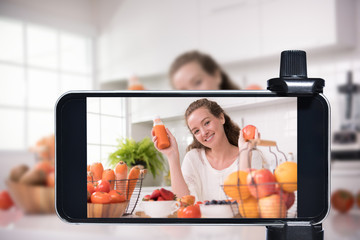 Young female blogger and vlogger and online influencer live streaming a cooking show on social media using a smartphone