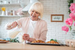 © Roman - Cooking with love. Attractive old woman cooking on kitchen. Cheerful grandmother is baking. Pours milk from a jug