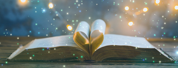 old opened book, heart shaped paper sheets, dark background with stars toned vintage selective focus
