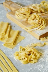 Homemade italian pasta, ravioli, fettuccine, tagliatelle on a wooden board and on a blue background. The cooking process, raw pasta. Tasty raw ravioli with ricotta and spinach,with flour on background