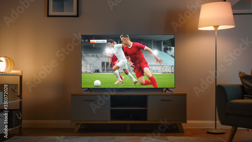 Shot of a TV with Soccer Match. Cozy Evening Living Room with a Chair and Lamps Turned On at Home.