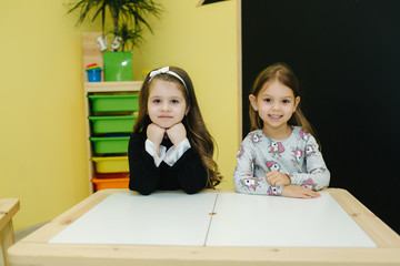 Girls are sitting at the table in kindergarden. Two girls friends