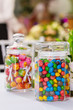 in the foreground is a glass jar with multi-colored sweets of oval-shaped dragee, in the background a glass jar with lollipops in a flowered wrap, out of focus.