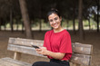 © Alberto Ortega  - Young attractive woman with glasses sitting in a bench and using her phone in a park, with a red shirt. Seville, Spain