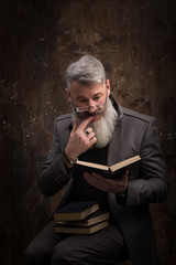 Portrait of a gray-haired bearded man with glasses reading book in Russian, on the cover Russian inscription M. Gorky, selective focus