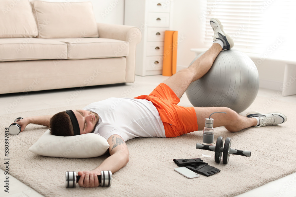 Lazy young man with sport equipment sleeping on floor at home - obrazy, fototapety, plakaty 