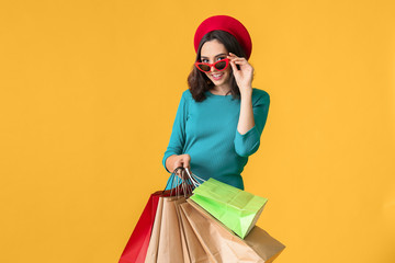 Poster - Beautiful young woman with shopping bags on color background