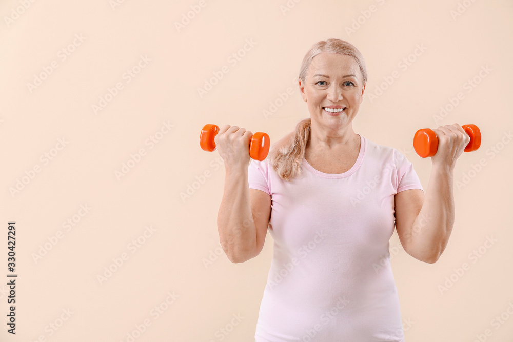 Sporty mature woman with dumbbells on light background