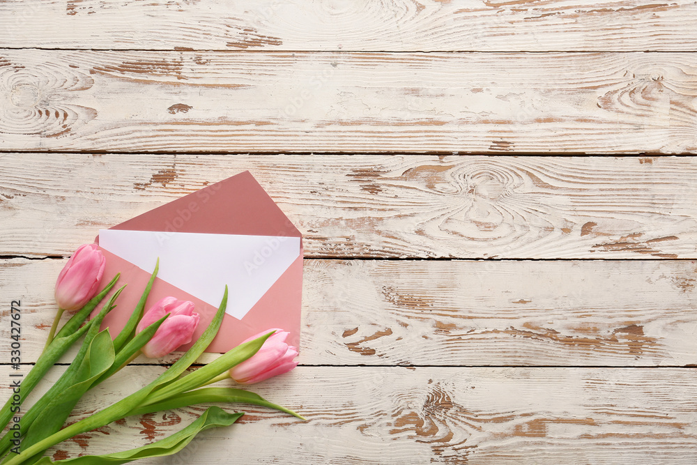 Envelope with card and flowers on white wooden background