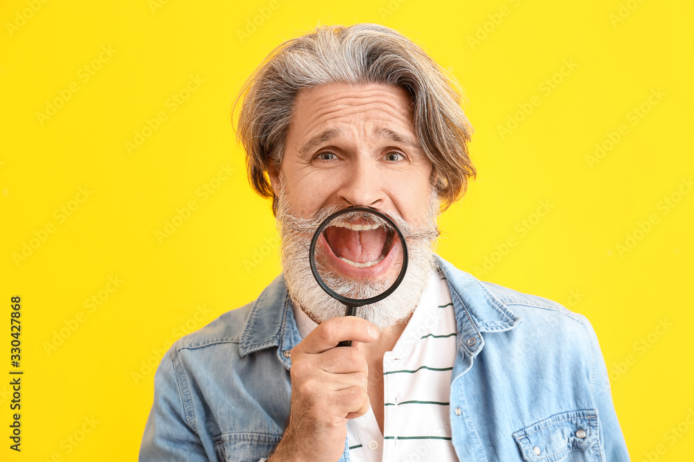 Funny elderly man with magnifier on color background
