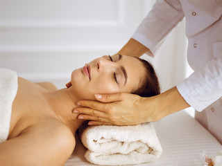 Beautiful brunette woman enjoying facial massage with closed eyes. Relaxing treatment in medicine and spa center concepts