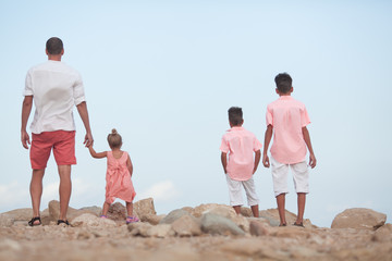 Big happy family walking at the beach. Dad and three children. The blue sky, the sun, fresh sea wind. Pleasure from nature and communication.