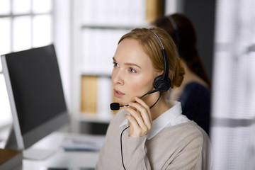 Businesswoman talking by headset while sitting in office. Call center and diverse people group in business