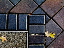 Interlocking Patio Stone Brick Paving Block Background Image With Metal Divider Strip. Yellow Leaves In The Fall. Patterns And Textures. Autumn Mood. Metal Divider Strip. Patterns