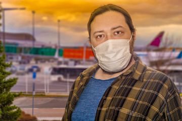 A tinted image of a man in a protective mask stands at the airport against the background of airplanes. The concept is the closure of borders between countries due to the risk of virus infection.