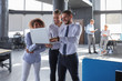 © ty - Group of modern business people are working using laptop and smiling while standing in the office hallway