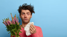 Indoor Shot Of Puzzled Man Holds Handkerhchief, Has Runny Nose And Other Symptoms Of Allergy, Allergic Reaction On Plant, Has Unbelievable Gaze At Camea, Cannot Stop Sneezing, Isolated On Blue Wall