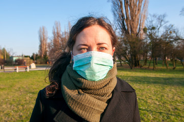 Portrait of a caucasian brunette woman in park in protective medical mask on face protection for spreading of disease virus SARS-CoV-2, Coronavirus, COVID-19